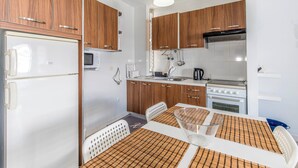 A compact kitchen with wooden cabinets, a white refrigerator, a microwave, a stove, and a dining table with a placemat. - Sunny Apartment with Terrace in El Médano (El Medano)