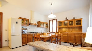 Una cocina con armarios de madera, un refrigerador blanco, una mesa de comedor con sillas y una lámpara colgante.