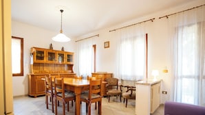 Un comedor con una mesa y sillas de madera, un aparador con puertas de cristal y un escritorio pequeño con una lámpara.