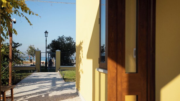 Un sendero lleva a un edificio amarillo con puerta de madera, una banca y un farol.