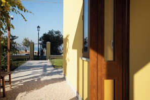 A pathway leading to a yellow building with a wooden door, a bench, and a lamp post.