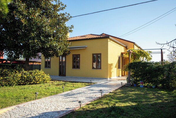 A yellow building with a tiled roof, a paved pathway, and a well-maintained garden with yellow flowers.