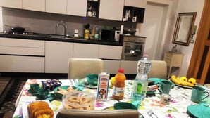 Mesa con comida y bebidas, una cocina al fondo y una silla en primer plano.