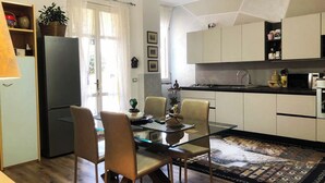 Una cocina moderna con armarios blancos, un refrigerador negro y una mesa de comedor de vidrio con sillas.