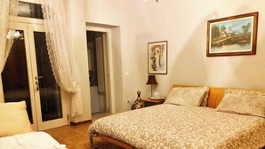 Un dormitorio con cama, una silla, una mesita de noche, una lámpara y un cuadro en la pared.