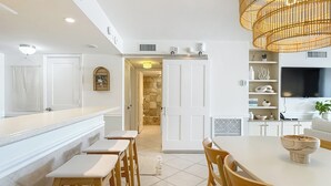 Una cucina moderna con isola centrale, sedie di legno, tavolo da pranzo e un grande televisore.