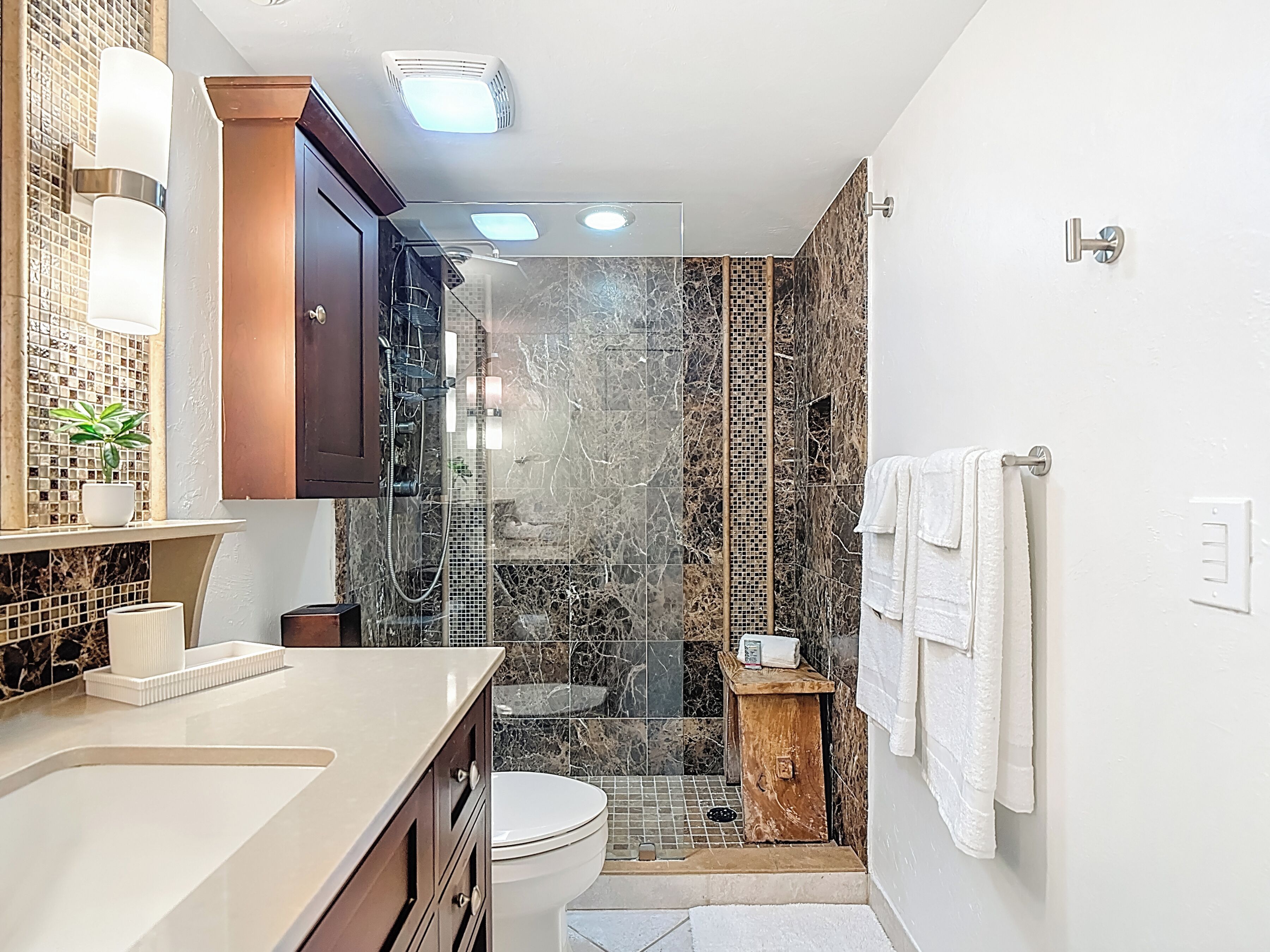 Ein modernes Badezimmer mit einer Marmordusche, einer Toilette, einem Waschbecken mit Spiegel und einem Handtuchhalter.