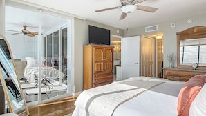 Una camera da letto con un letto, un armadio, uno specchio, una ventola a soffitto e una porta scorrevole in vetro che dà su un balcone.