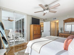 A bedroom with a bed, a wardrobe, a mirror, a ceiling fan, and a sliding glass door leading to a balcony. - Beachfront Getaway at Caper Beach Club #803 | Private Chiller/Heated Pool (Fort Myers Beach)