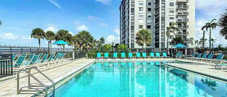 A swimming pool with lounge chairs and a tall building in the background.
