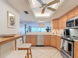 A modern kitchen with wooden cabinets, a stainless steel oven, a microwave, and a ceiling fan. - Beachfront Getaway at Caper Beach Club #803 | Private Chiller/Heated Pool (Fort Myers Beach)