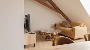 Un dormitorio tipo loft moderno con vigas de madera a la vista, una mesa de centro de vidrio, un sofá y un televisor.