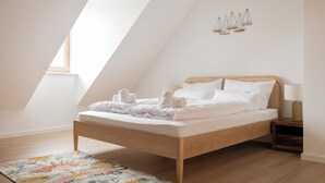 Un dormitorio con techo inclinado, estructura de cama de madera, ropa de cama blanca, lámpara de noche y un adorno en la pared.