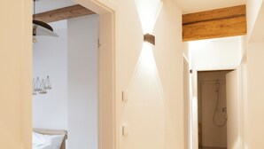 Un pasillo con vigas de madera, una cama con ropa blanca y una zona de ducha.