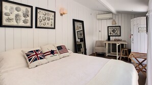 Une chambre avec un grand lit, une petite table et une chaise. Il y a des tableaux encadrés au mur et une pancarte sur la porte.