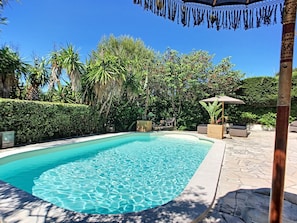 Una piscina con superficie d'acqua cristallina e blu, circondata da vegetazione lussureggiante e un'area patio in pietra.