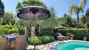 Un espace aménagé au bord de la piscine, avec une table à manger, des chaises et un parasol.