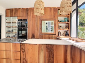 Une cuisine moderne avec des meubles en bois, des appareils électroménagers intégrés et une grande fenêtre offrant une vue sur l’extérieur.