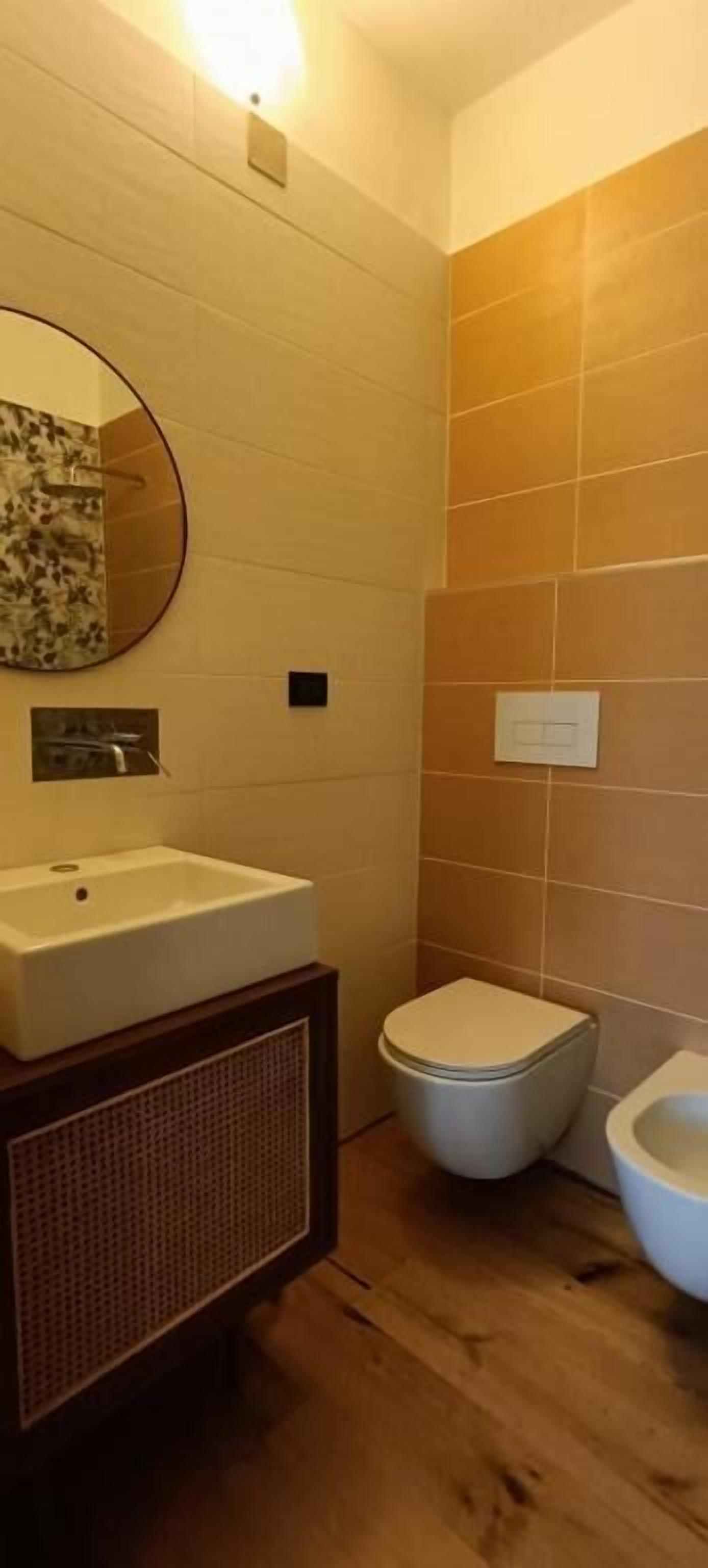 A bathroom with a wooden floor, a white sink, a toilet, and a bidet.