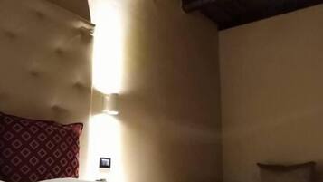 Habitación de hotel con techo de madera, cama con colcha estampada y mesita de noche con lámpara.