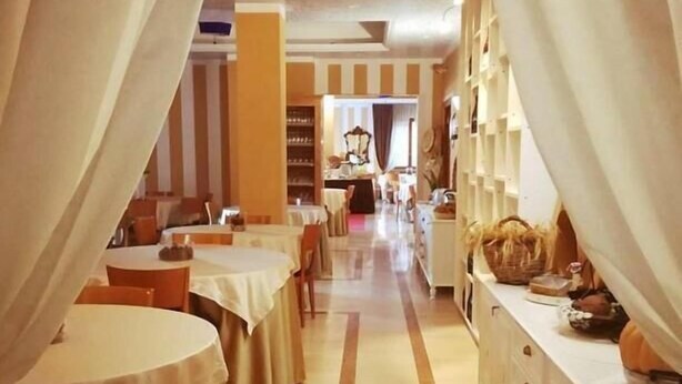 A hotel corridor with tables and chairs, a buffet area, and a mirror. - HOTEL ARIMANNIA (Caramanico Terme)