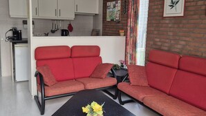 Ein gemütlicher Wohnbereich mit einem roten Sofa, einem kleinen Tisch mit Blumen und einer Küchenzeile im Hintergrund.