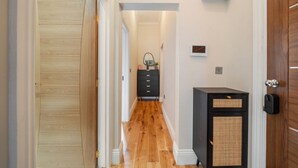 A hallway with wooden flooring, a black cabinet, and a door with a handle. - Argyl | Cambridge Gardens: Apt. B (Greater London)
