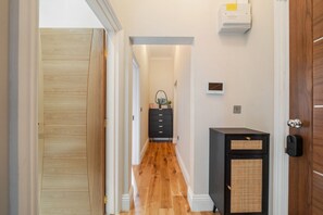 A hallway with wooden flooring, a black cabinet, and a door with a handle. - Argyl | Cambridge Gardens: Apt. B (Greater London)