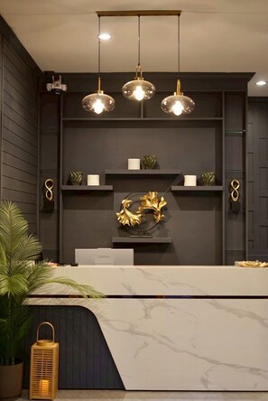 Un comptoir d’accueil avec un plateau en marbre, trois lampes suspendues et des objets décoratifs disposés sur des étagères.