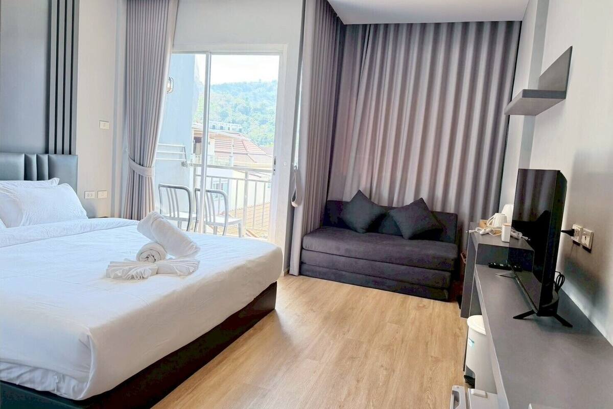 A hotel room with a bed, a sofa, a TV, and a balcony with curtains.