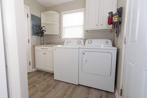 A laundry area with a washing machine and dryer, a window with blinds, and a vase with flowers on the counter. - Pet-Friendly Cozy Cape Escape Near Beach (Lower Township)