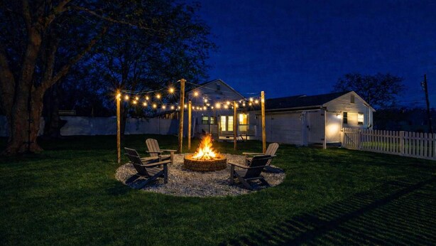 A backyard with a fire pit and string lights, surrounded by chairs, and a house in the background. - Pet-Friendly Cozy Cape Escape Near Beach (Lower Township)