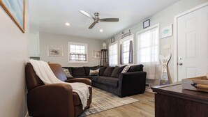 A living room with a brown leather chair, a dark brown sofa, and a wooden coffee table. There is a ceiling fan, a rug, and a door with a 'WE' sign. - Pet-Friendly Cozy Cape Escape Near Beach (Lower Township)