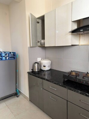 Une cuisine compacte équipée d’une cuisinière à gaz, d’une bouilloire et d’un cuiseur à riz, le tout posé sur le plan de travail.