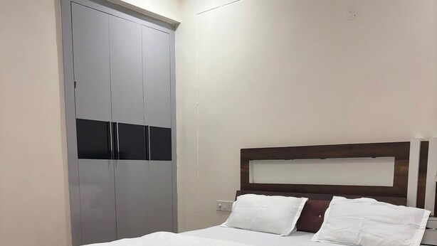 A bedroom with a large bed, wooden headboard, and a grey wardrobe. - Twin Nest 2BHK | AC |Gated | Near Chandigarh Univ. (Mohali)