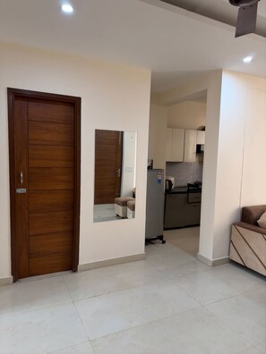 Une chambre moderne avec une porte en bois, un petit miroir, une kitchenette équipée de placards et un canapé.
