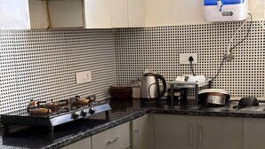 A kitchen with a black countertop, stainless steel appliances, and a water dispenser. - Twin Nest 2BHK | AC |Gated | Near Chandigarh Univ. (Mohali)