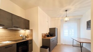 A modern kitchen with dark cabinets, a wooden countertop, and a built-in oven. There is a small trash bin and a dining area with a table and chairs. - ღLiboria | Villa Münter (Murnau am Staffelsee)