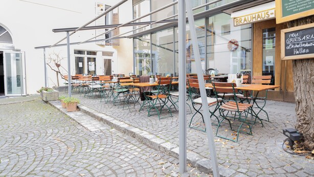An outdoor seating area with tables and chairs, a sign for 'BRAUHAUS', and a tree. - ღLiboria | Villa Münter (Murnau am Staffelsee)