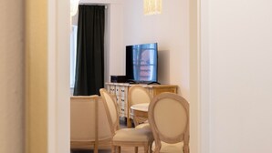 A room with a wooden floor, a television on a wooden stand, and a chandelier. - ღLiboria | Villa Münter (Murnau am Staffelsee)