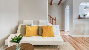 Ein weißes Sofa mit gelben Kissen, ein Holztisch und eine Pflanze in einer Glasvase.