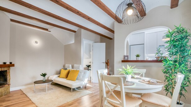Ein modernes Wohnzimmer mit einem weißen Sofa, Holzboden, einem Esstisch mit Stühlen, einem Kamin und einer großen Pflanze.