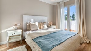 Ein Schlafzimmer mit einem großen Bett, einem Nachttisch mit Lampe, einem Fenster mit Vorhängen und Blick ins Grüne.