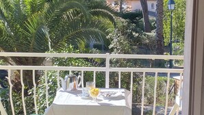 Ein Balkon mit Tisch für zwei Personen, umgeben von viel Grün und Blick auf Bäume und Gebäude.