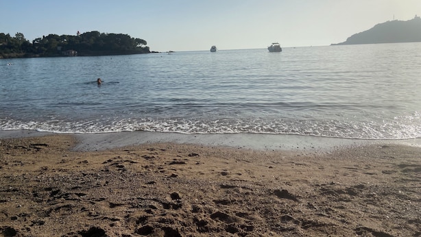 Ein Strand mit sandigem Ufer, ruhigem Wasser und Booten in der Ferne.