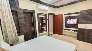 A hotel room with a bed, a TV mounted on the wall, a wardrobe, and a door. - hotel nandini palace (Varanasi)