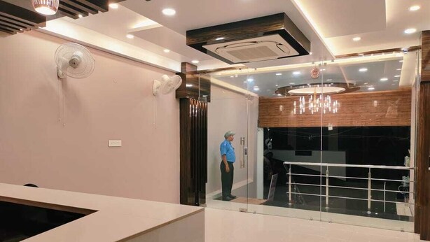 A modern hotel lobby with a reception desk, a glass partition, and a person standing near the entrance. - hotel nandini palace (Varanasi)