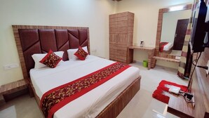A hotel room with a large bed, wooden headboard, a wardrobe, a vanity with a mirror, and a red rug. - hotel nandini palace (Varanasi)