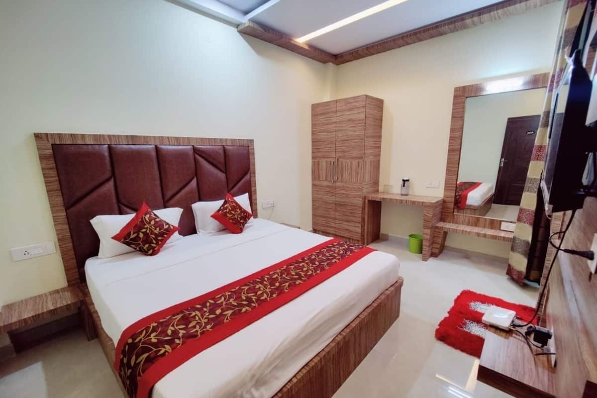 A hotel room with a large bed, wooden headboard, a wardrobe, a vanity with a mirror, and a red rug.