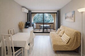 A room with a dining table and chairs, a sofa, a TV, and a large window with a view of trees. - Peaceful apartment with pool in Saint-Cyprien (Saint-Cyprien)